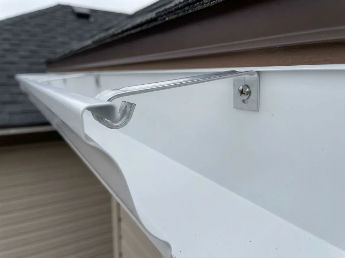 Close-up inside an eavestrough showing a single aluminum hidden hanger hooked under the front lip, with its screw passing through the back into the fascia.
